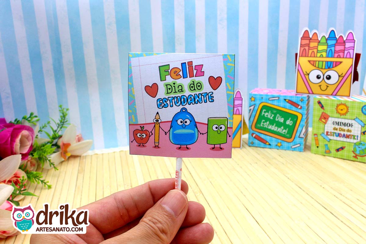 Capinha de pirulito do Dia do Estudante com personagens escolares em estilo cartoon e fundo azul listrado