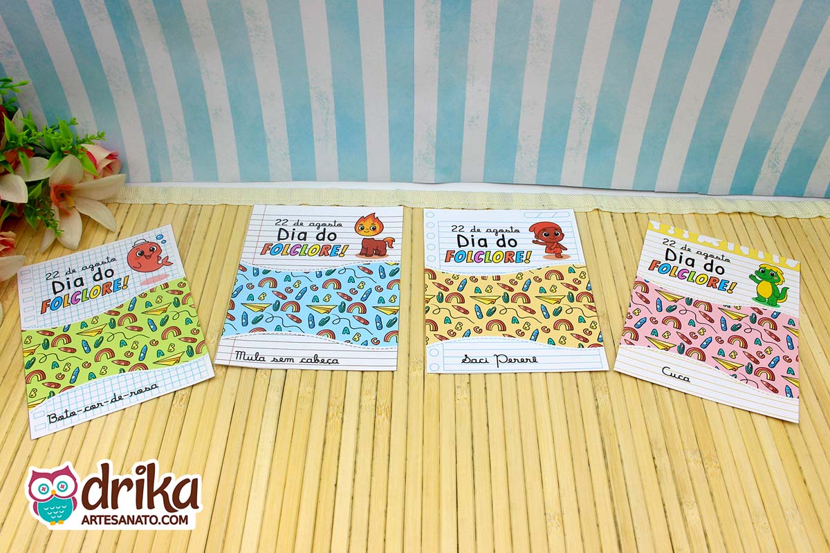 Quatro cartões porta-bombom do Dia do Folclore com personagens em estilo caderno escolar sobre mesa de bambu
