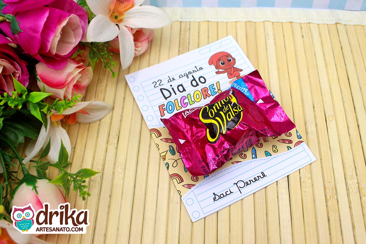 Cartão do Saci Pererê com Sonho de Valsa sobre mesa de bambu, com flores ao lado.