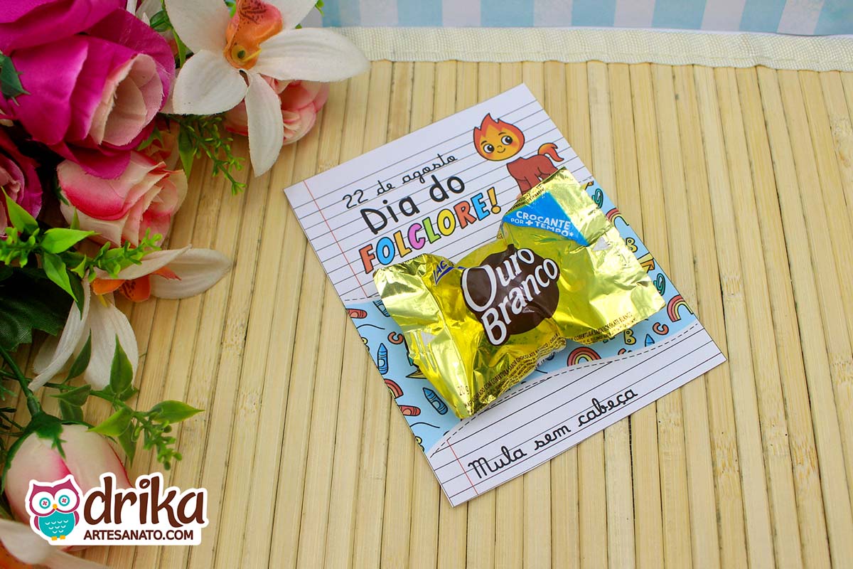 Cartão porta-bombom da Mula sem Cabeça com bombom Ouro Branco, sobre mesa de bambu e flores.