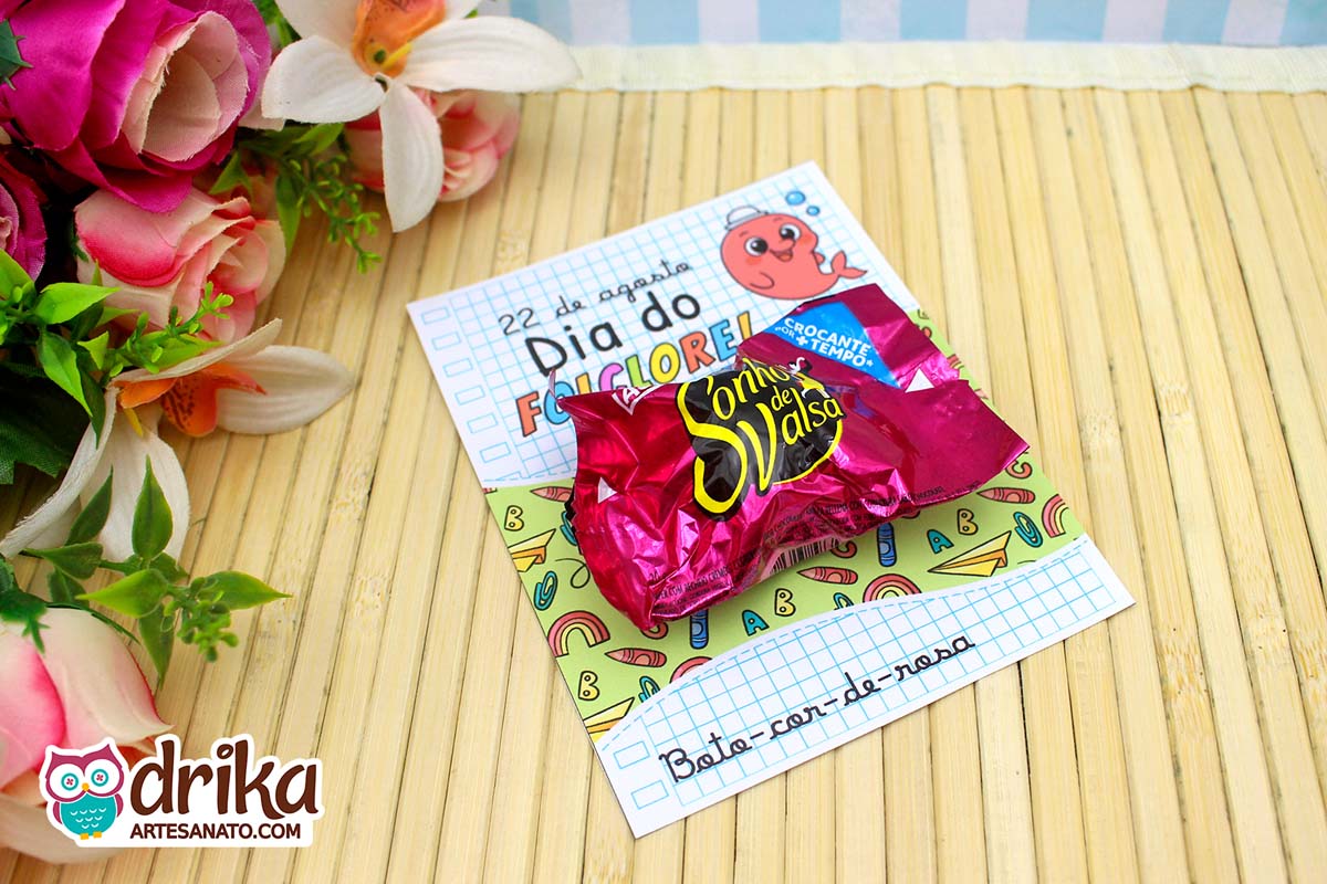 Cartão porta-bombom do Boto-cor-de-rosa com bombom Sonho de Valsa, sobre mesa de bambu e flores.