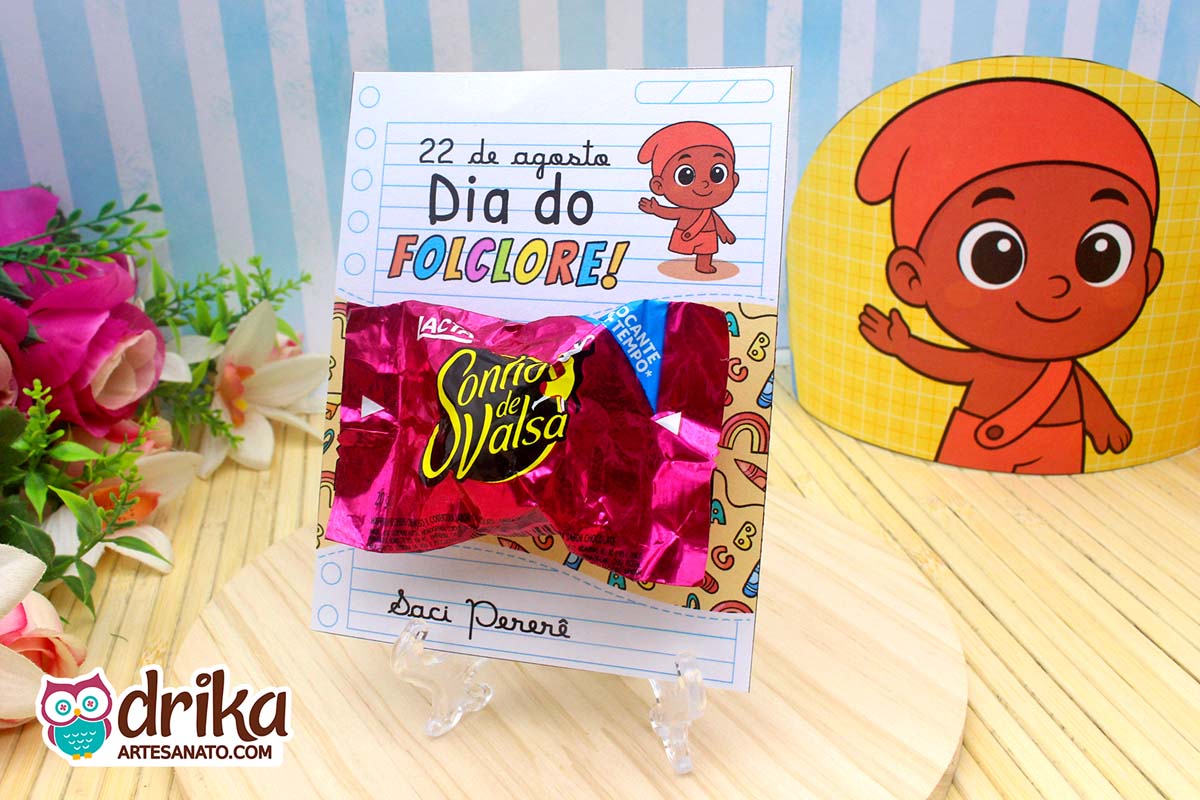 Cartão porta-bombom do Saci Pererê com bombom Sonho de Valsa em suporte transparente sobre mesa de madeira