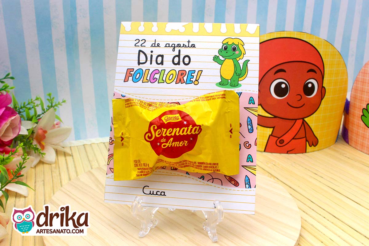 Cartão porta-bombom da Cuca com bombom Serenata de Amor em suporte transparente sobre madeira