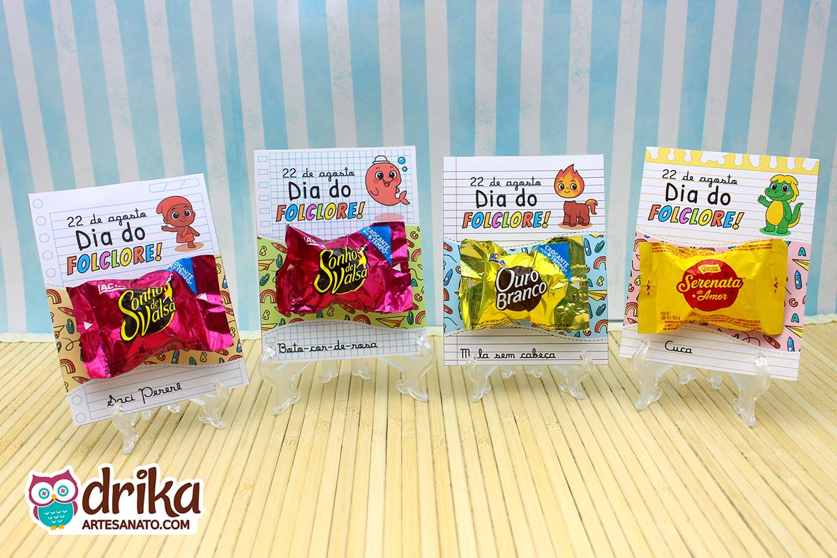 Quatro cartões porta-bombom do folclore brasileiro em suportes transparentes sobre mesa clara.