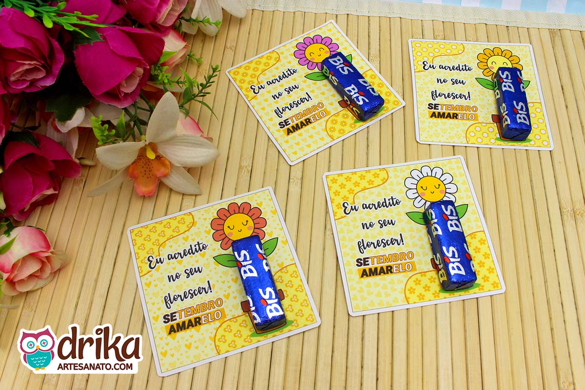 Visão superior de quatro cartões porta-bis de flor com chocolate Bis, em fundo de bambu claro.