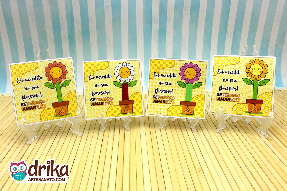 Quatro cartões porta-lixa de flor do Setembro Amarelo lado a lado em suportes transparentes sobre esteira de bambu.