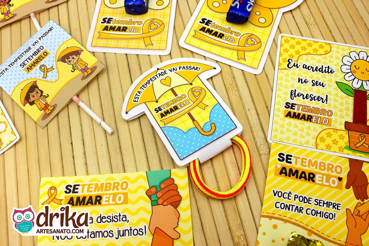 Porta-xuxinha guarda-chuva azul em meio a outras lembrancinhas amarelas do Setembro Amarelo sobre mesa de bambu.