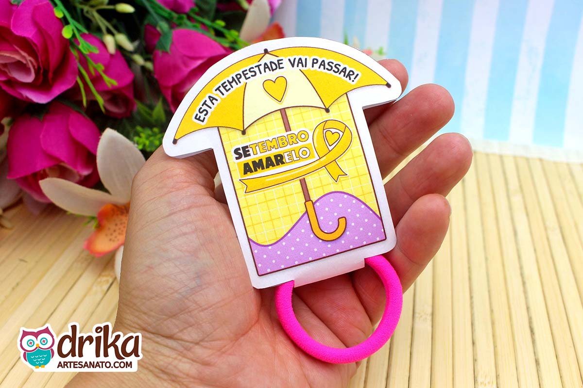 Porta-xuxinha guarda-chuva amarelo e lilás do Setembro Amarelo com xuxinha rosa na mão.
