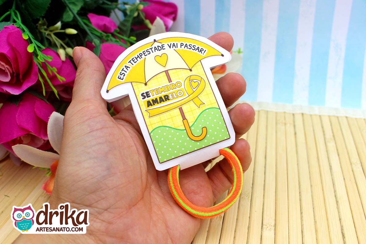 Porta-xuxinha guarda-chuva amarelo e verde do Setembro Amarelo com xuxinha laranja e amarela na mão.