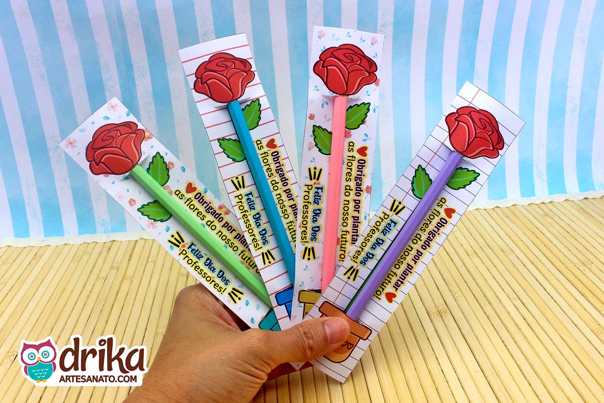 Mão segurando quatro cartões flor porta-lápis com rosas vermelhas e mensagens de agradecimento em fundo de madeira claro.