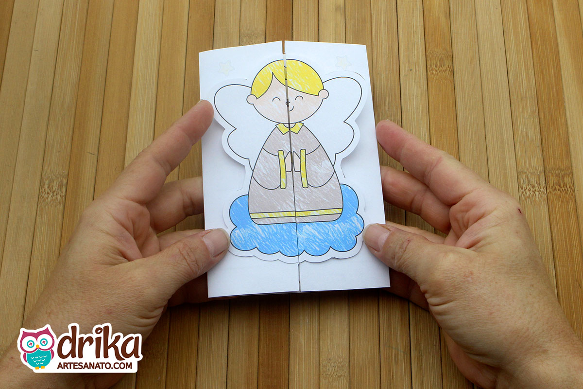 Mãos segurando cartão de Natal fechado com desenho de anjo loiro sobre nuvem azul