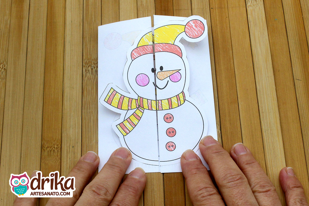 Cartão de Natal interativo com boneco de neve colorido sendo aberto sobre mesa de madeira