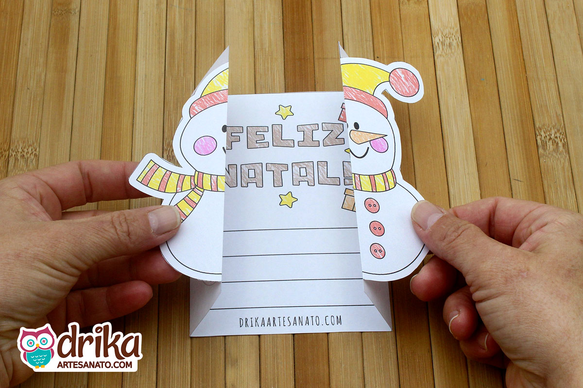 Mãos abrem cartão de Natal interativo com boneco de neve, revelando mensagem de "Feliz Natal"