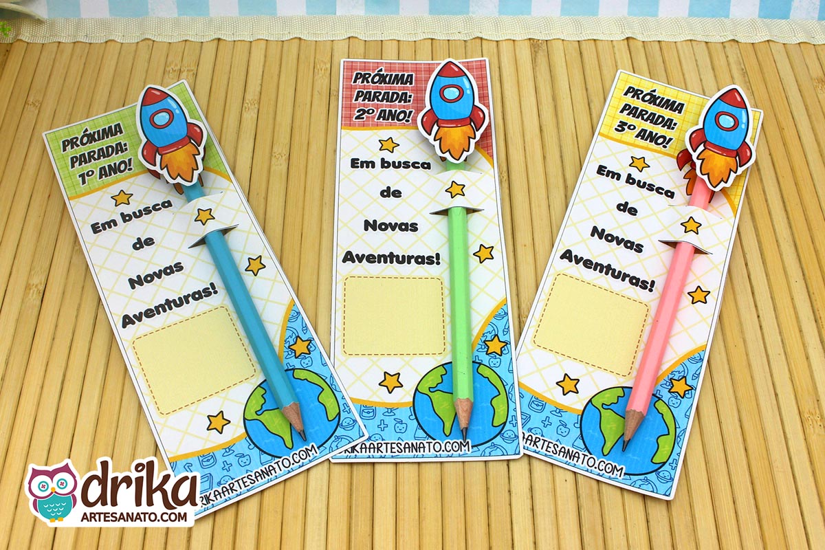 Visão superior de três cartões porta-lápis de foguete para 1º, 2º e 3º ano com lápis coloridos sobre fundo de madeira