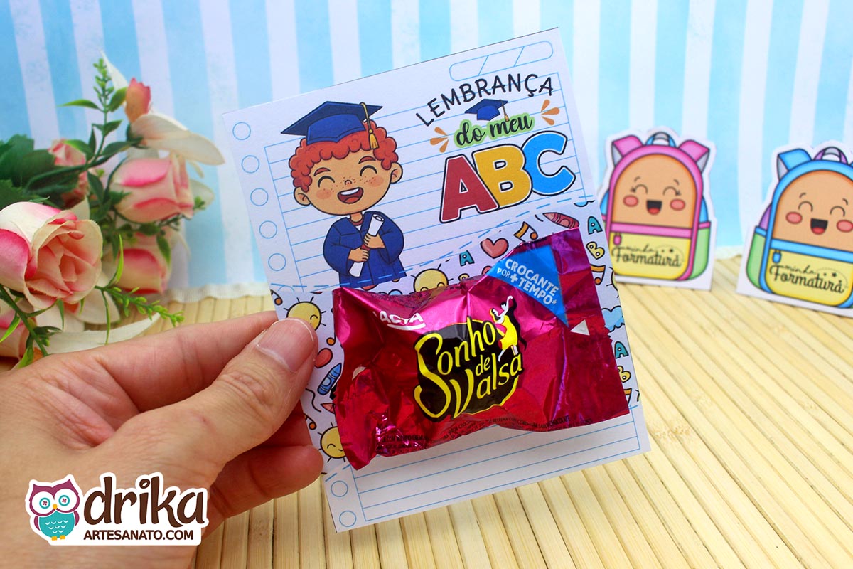 Mão segurando cartão porta-bombom de formatura ABC com menino ruivo e bombom Sonho de Valsa.