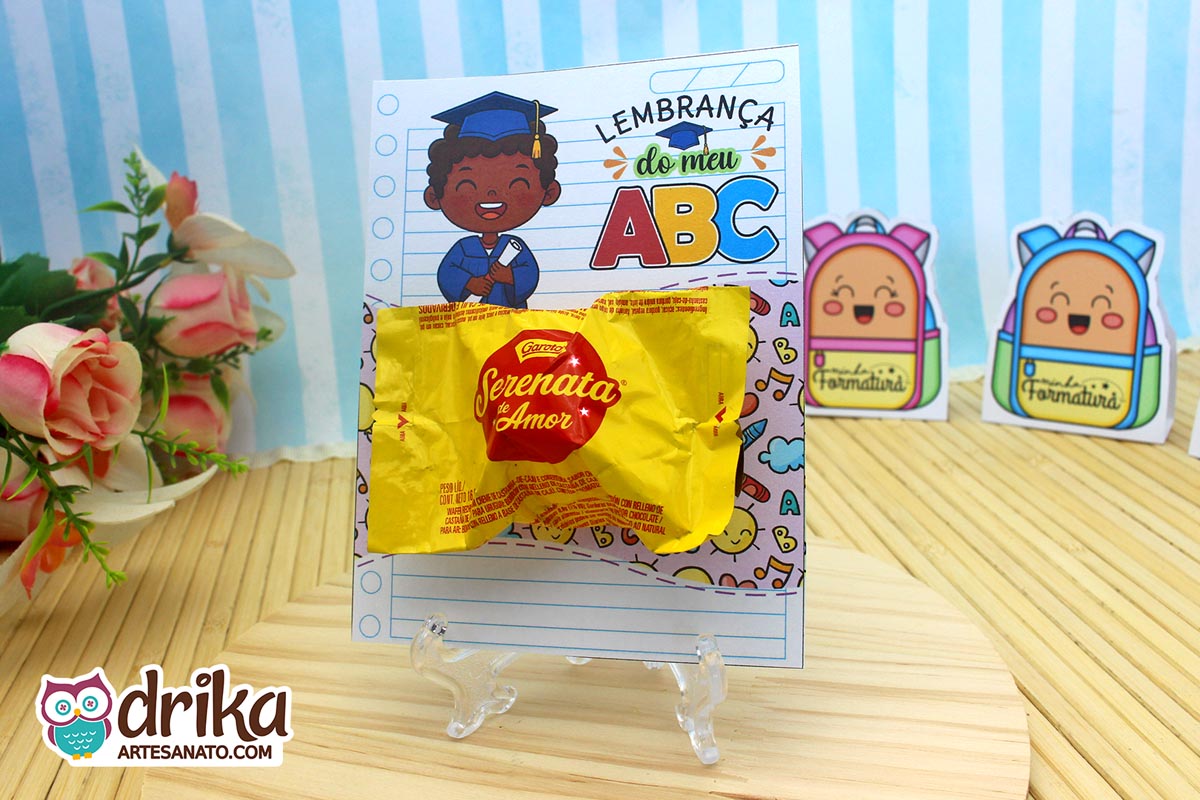 Cartão porta-bombom com menino negro de cabelo crespo e beca azul, segurando diploma, com bombom Serenata de Amor.