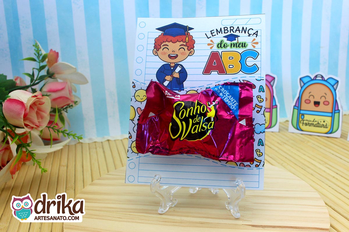 Cartão porta-bombom com menino ruivo de beca azul, segurando diploma, com bombom Sonho de Valsa.