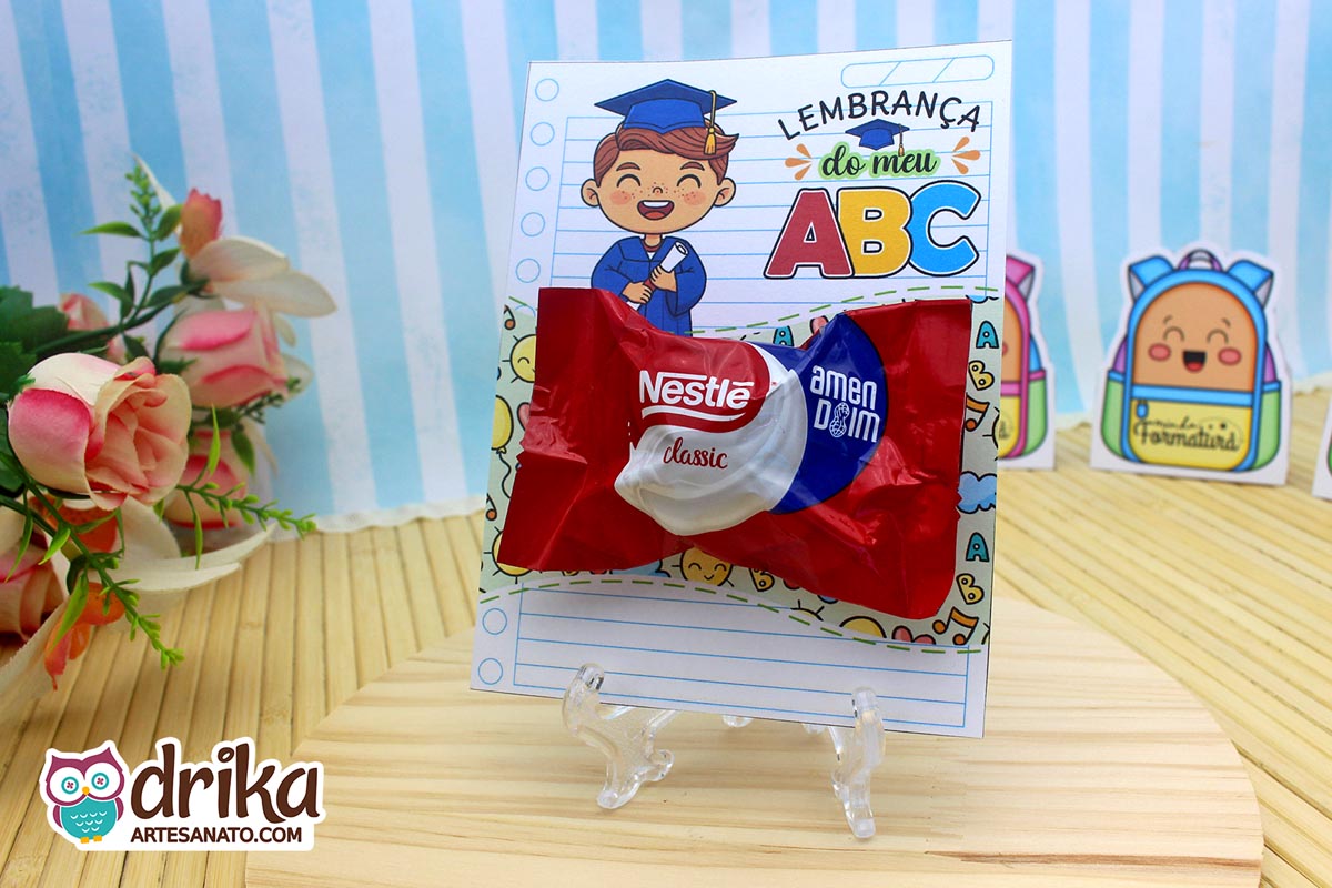 Cartão porta-bombom com menino castanho de beca azul, segurando diploma, com bombom Nestlé Classic.