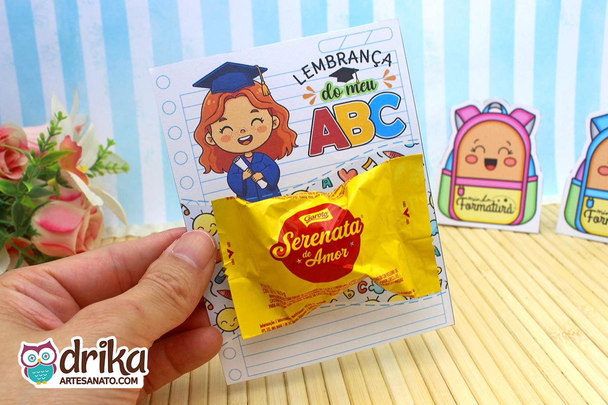 Mão segurando cartão porta-bombom de formatura ABC com menina ruiva e bombom Serenata de Amor