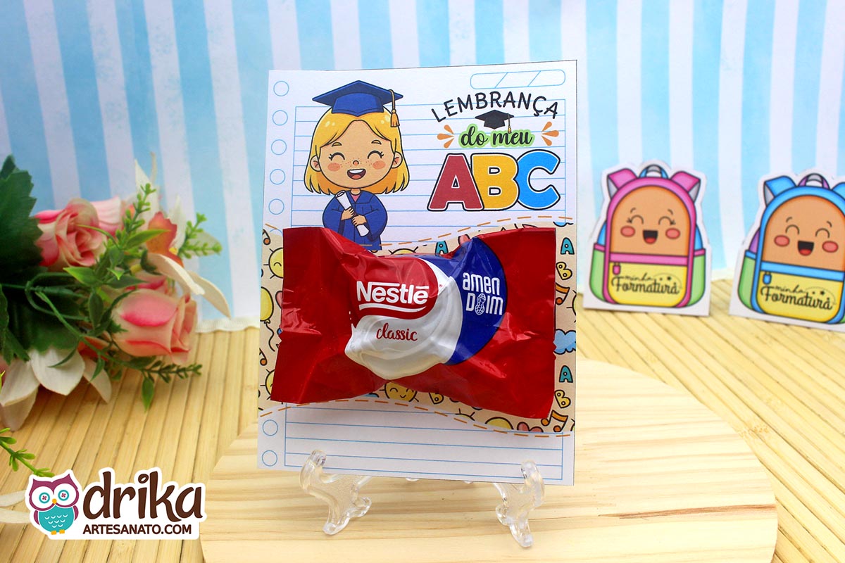 Cartão porta-bombom de formatura ABC com menina loira segurando diploma e bombom Sonho de Valsa em suporte transparente