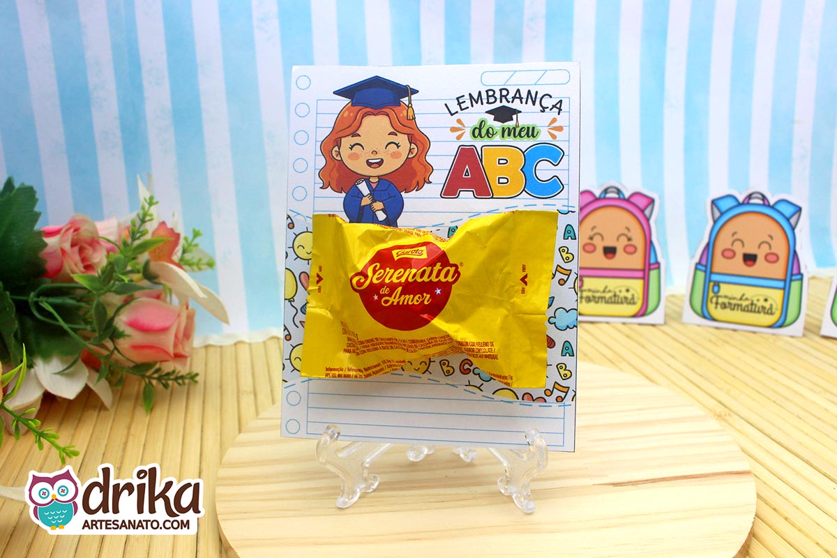 Cartão porta-bombom de formatura ABC com menina ruiva segurando diploma e bombom Serenata de Amor em suporte transparente