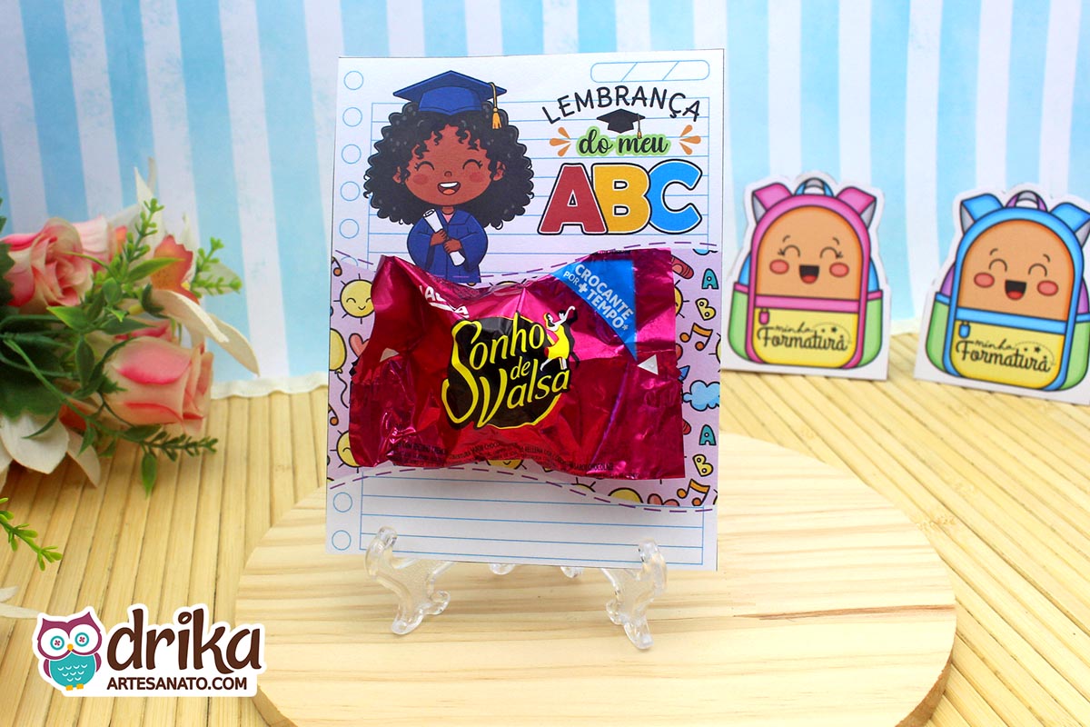 Cartão porta-bombom de formatura ABC com menina de cabelo crespo segurando diploma e bombom Sonho de Valsa em suporte transparente