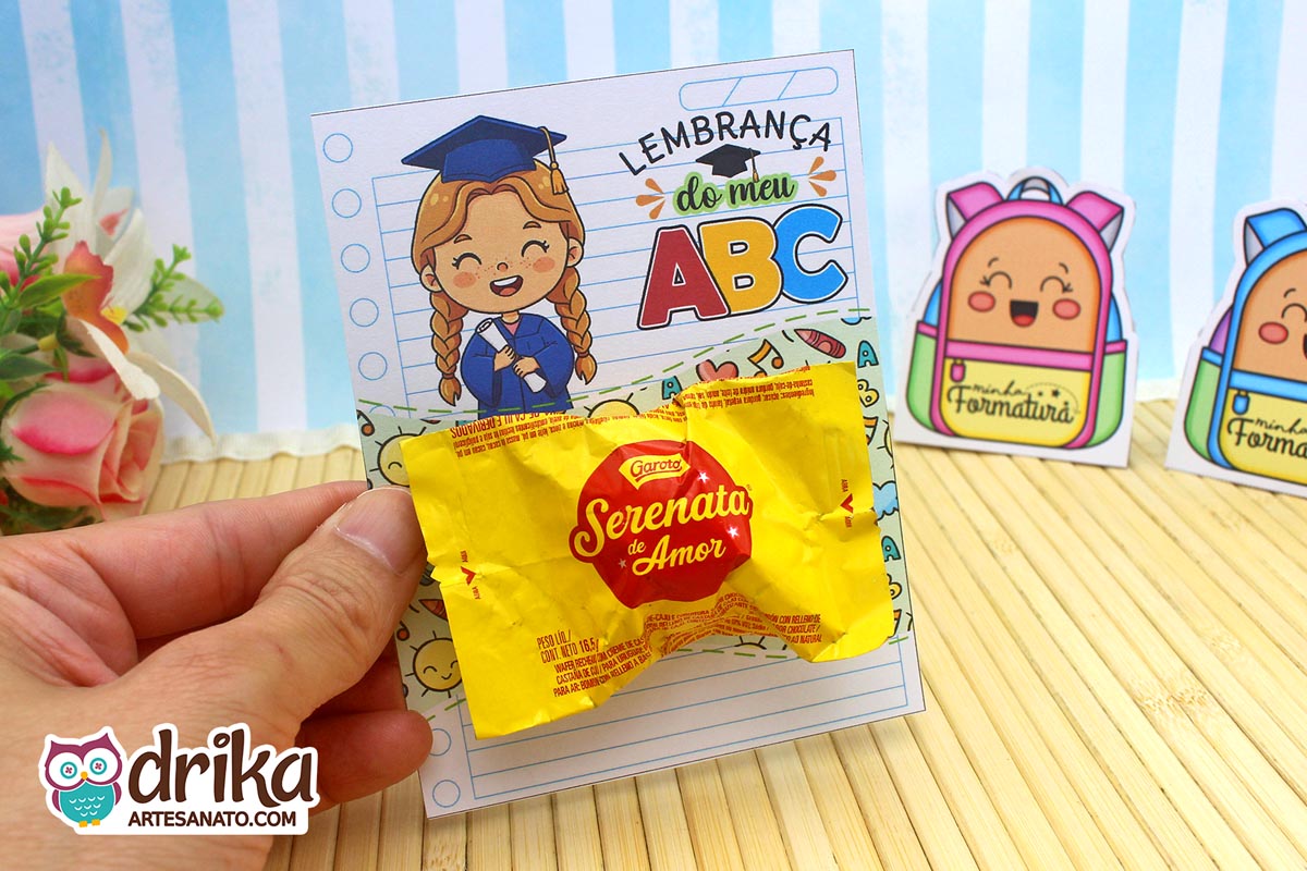 Mão segurando cartão porta-bombom Formatura ABC com menina de cabelo castanho e bombom Serenata de Amor