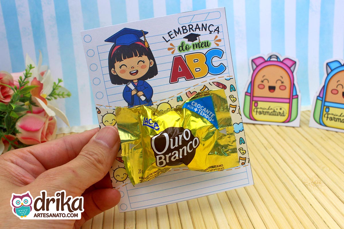 Mão segurando cartão porta-bombom Formatura ABC com menina de cabelo preto e bombom Ouro Branco