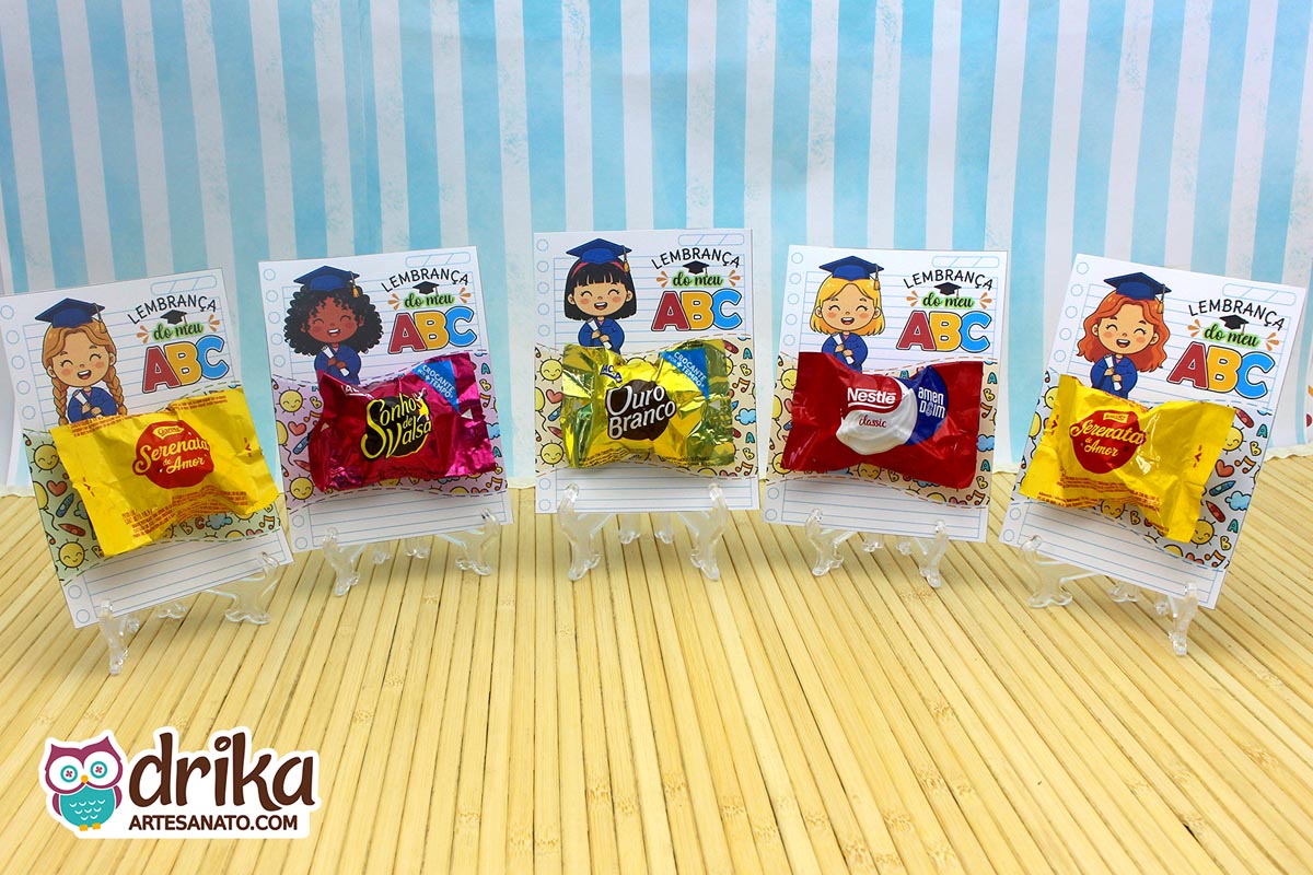 Cinco cartões porta-bombom Formatura ABC com meninas formandas de diferentes etnias e bombons variados em mini cavaletes transparentes.