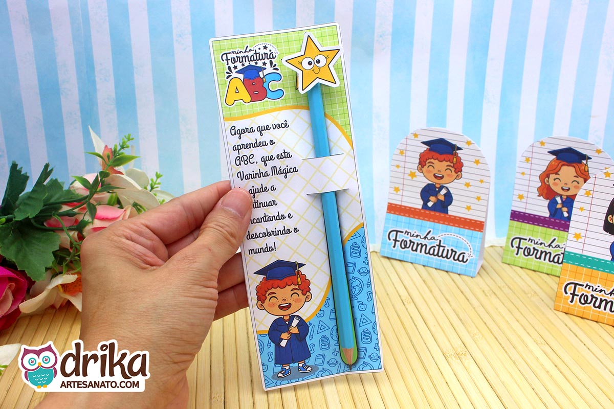 Mão segurando cartão porta-lápis formatura ABC com menino ruivo, lápis azul com estrela e mensagem inspiradora.