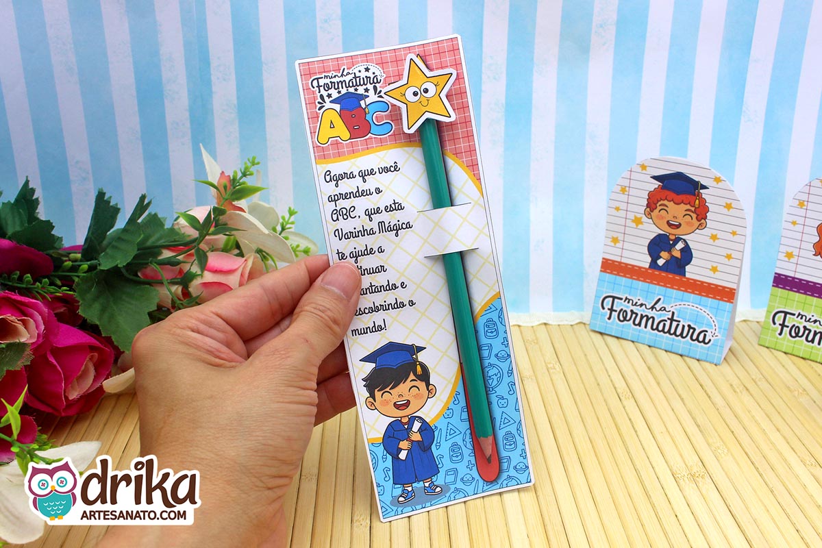 Mão segurando cartão porta-lápis Formatura ABC com menino de cabelo preto e lápis/varinha amarela.