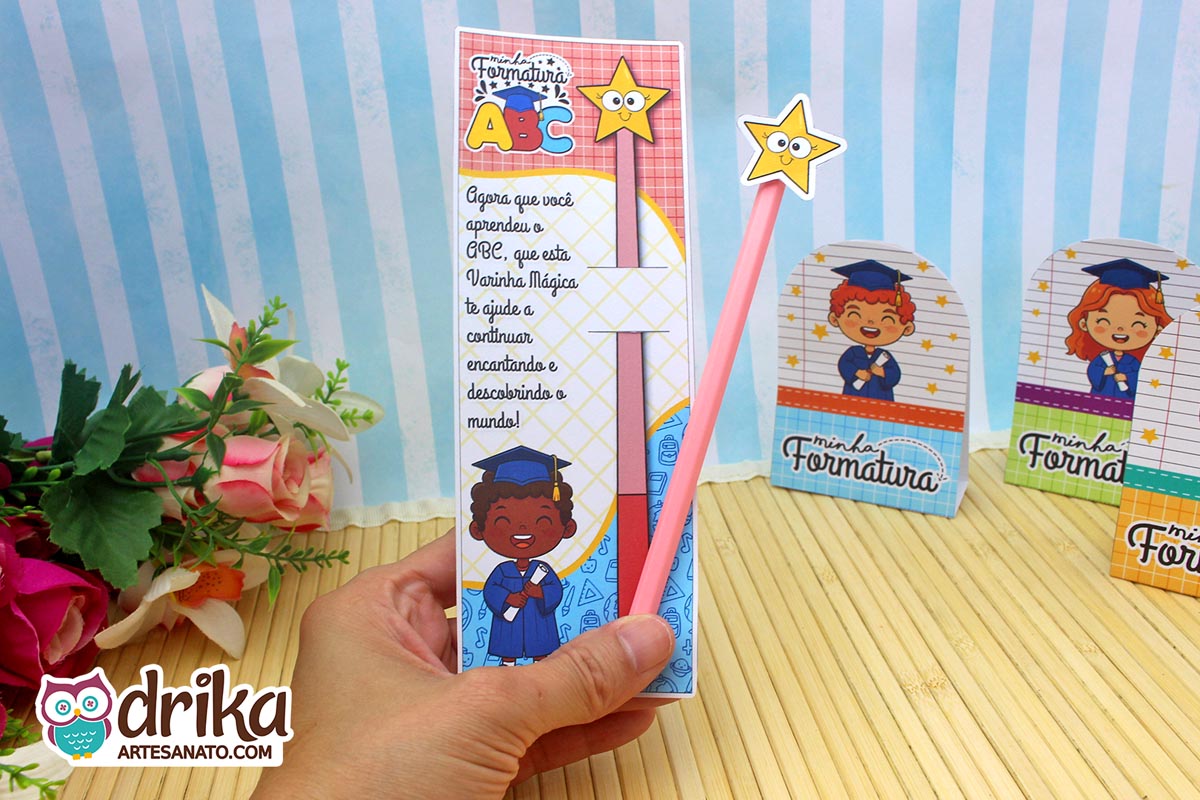 Cartão porta-lápis Formatura ABC com menino de cabelo crespo segurando diploma e lápis rosa com estrela sobre fundo floral.