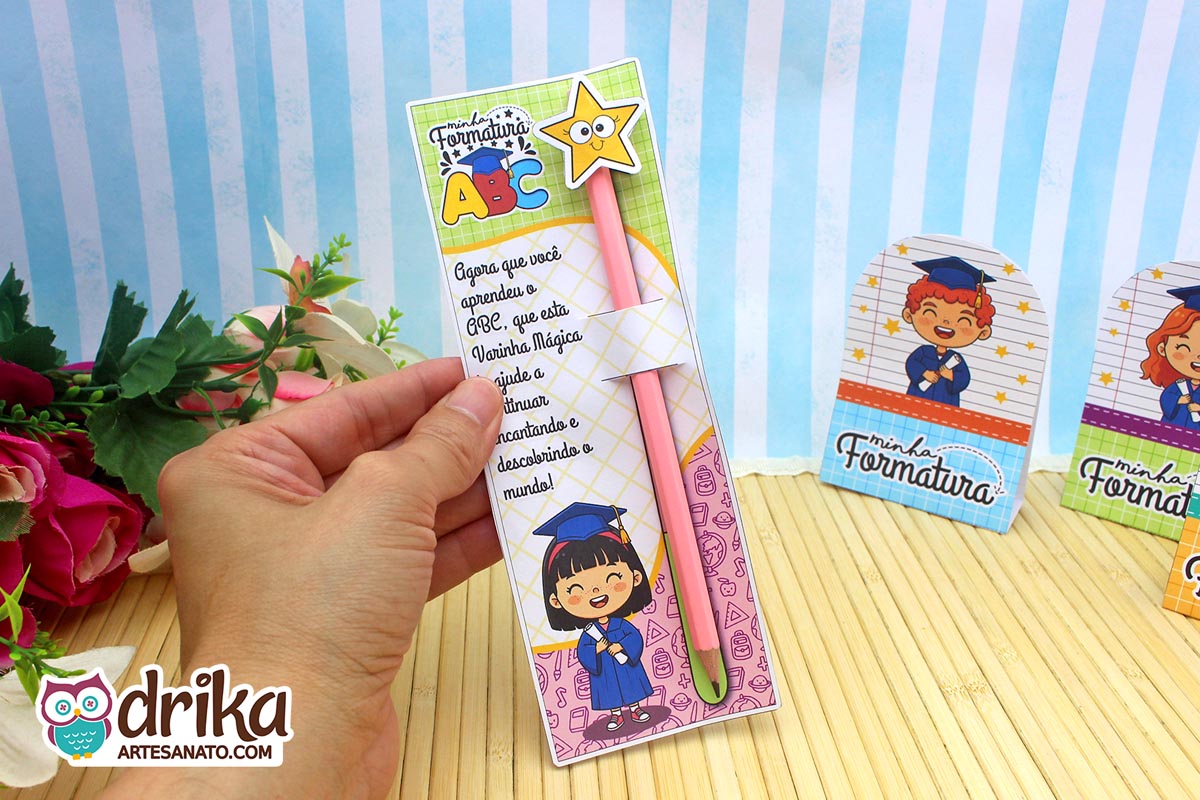 Mão segurando cartão formatura ABC com menina de cabelo preto, lápis branco com estrela, frase e desenhos.