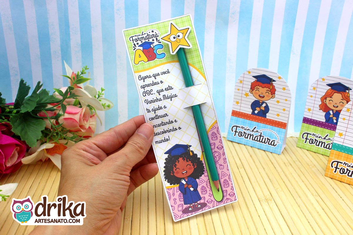 Mão segurando cartão formatura ABC com menina de cabelo crespo, lápis verde com estrela, frase e desenhos.