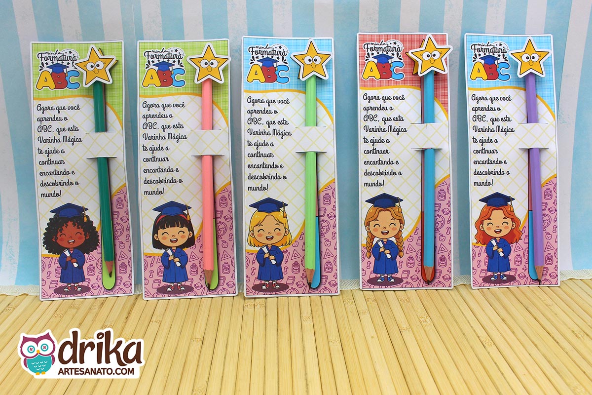 Visão superior de cinco cartões porta-lápis Formatura ABC com lápis/varinhas coloridos sobre mesa de madeira.