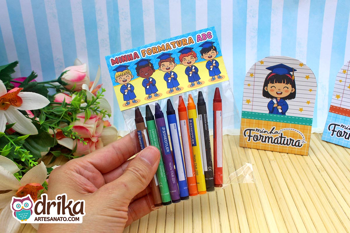 Mão segurando saquinho com giz de cera e lapela azul e amarela de formatura ABC com desenhos de formandos.