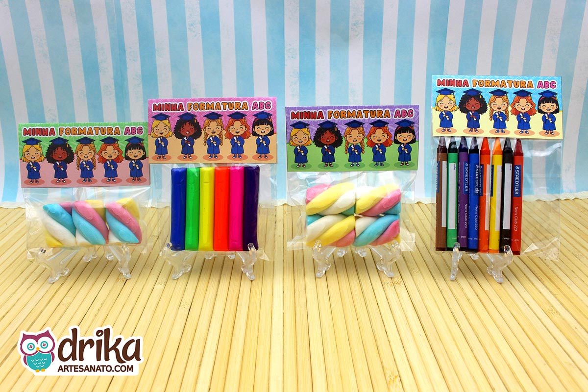 Quatro lembrancinhas de formatura ABC com lapelas e doces/lápis, em mini suportes sobre fundo listrado azul.