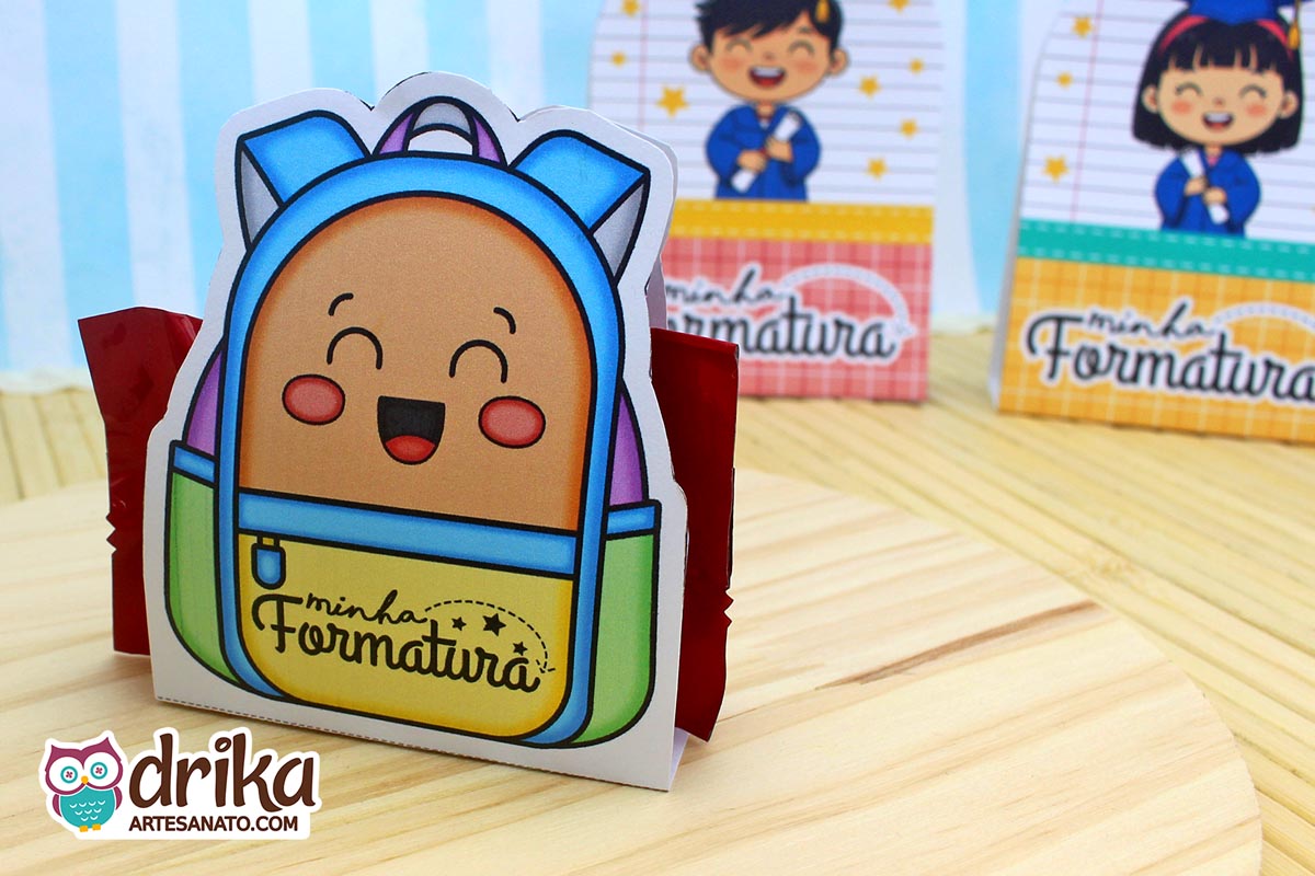 Mochila porta-bombom azul e amarela com rosto de menino sorrindo, bombom vermelho à mostra e outras lembrancinhas ao fundo