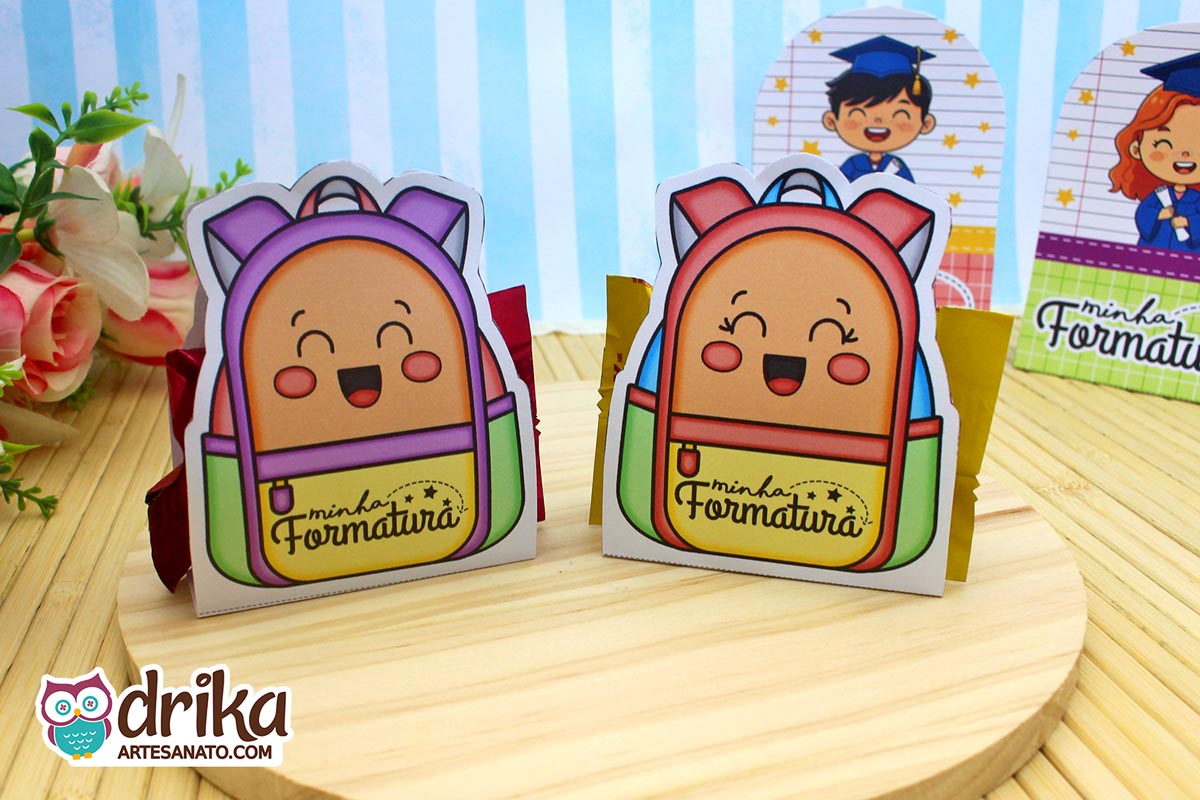 Mochilas porta-bombom de formatura ABC, uma roxa e outra vermelha, com rostinhos sorrindo sobre base de madeira.