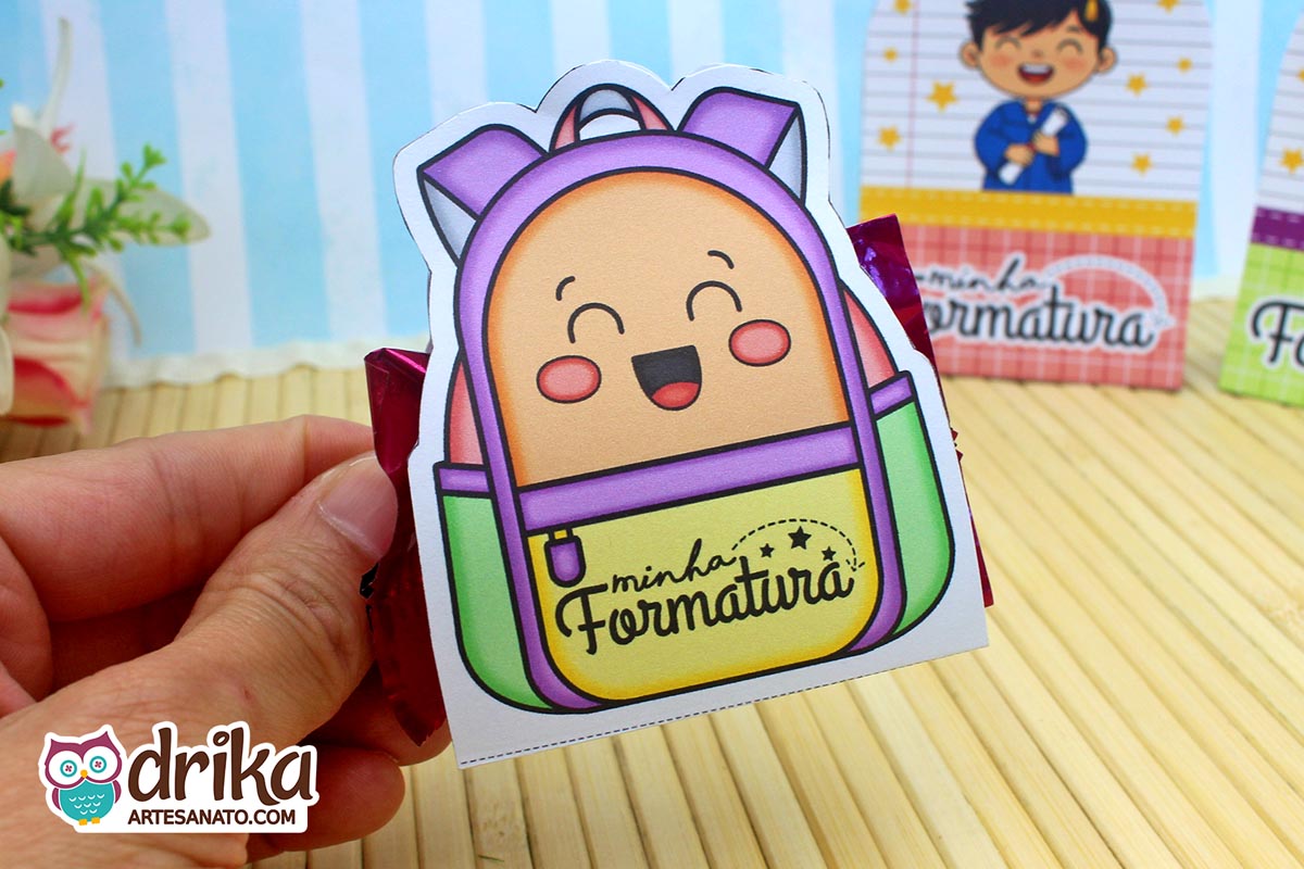 Mochila porta-bombom roxa e verde com rosto de menino sorrindo, segurada por mão, com bombom vermelho.