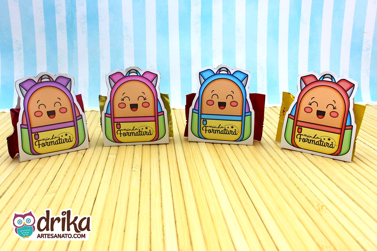 Quatro mochilas porta-bombom de formatura ABC com rostinhos sorrindo e cores variadas sobre fundo listrado azul e branco.