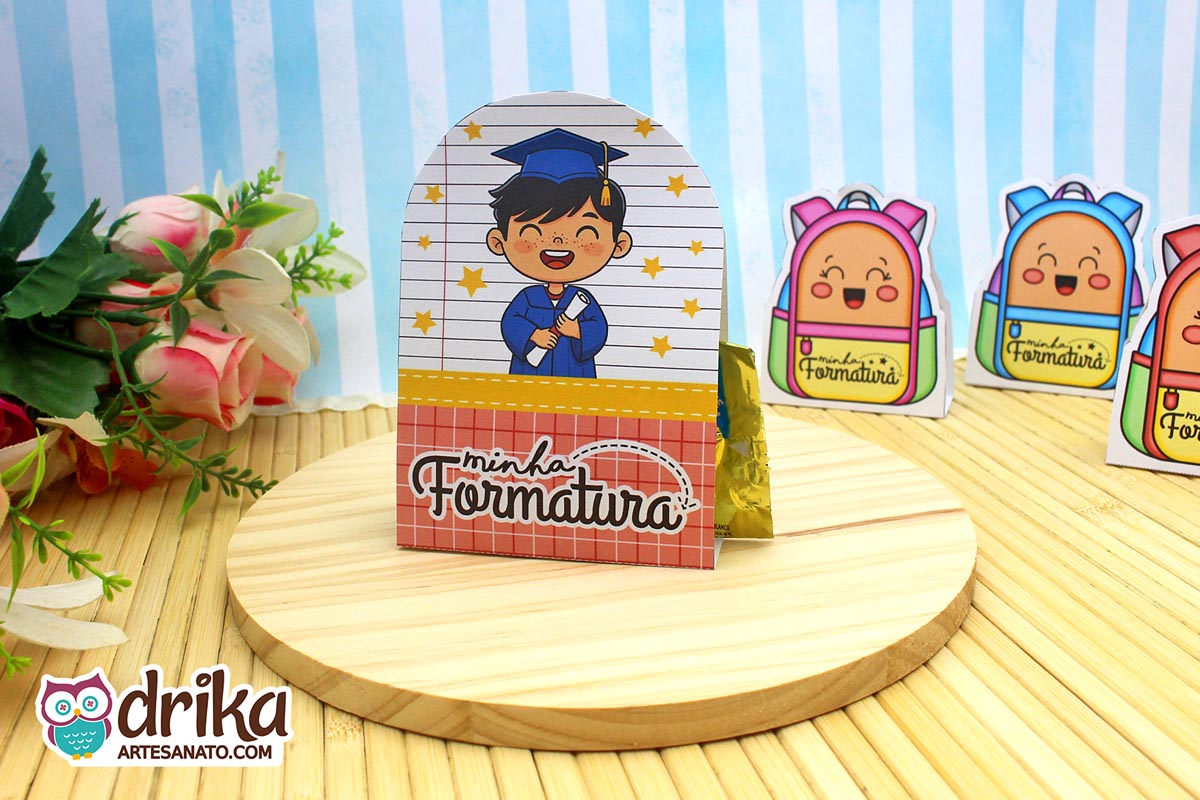 Porta-bombom formatura ABC com menino de cabelo preto, beca azul e capelo, segurando diploma, sobre base de madeira