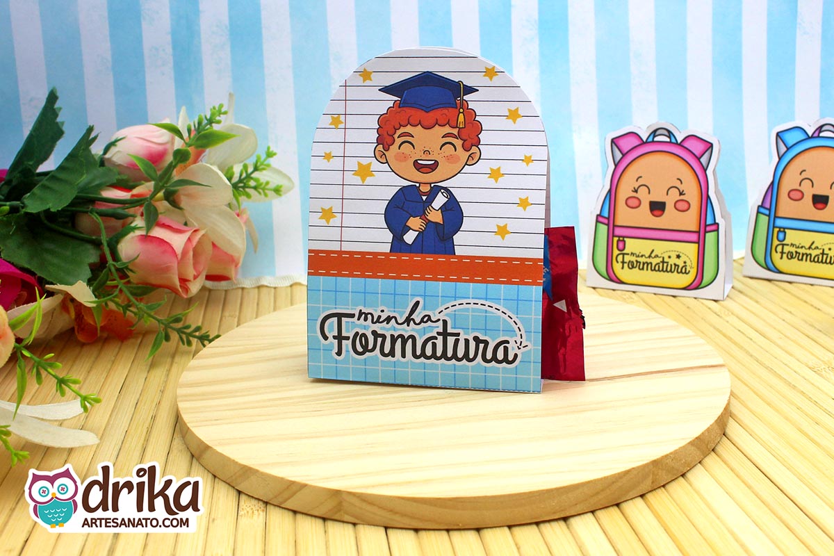 Porta-bombom formatura ABC com menino ruivo, beca azul e capelo, segurando diploma, sobre base de madeira
