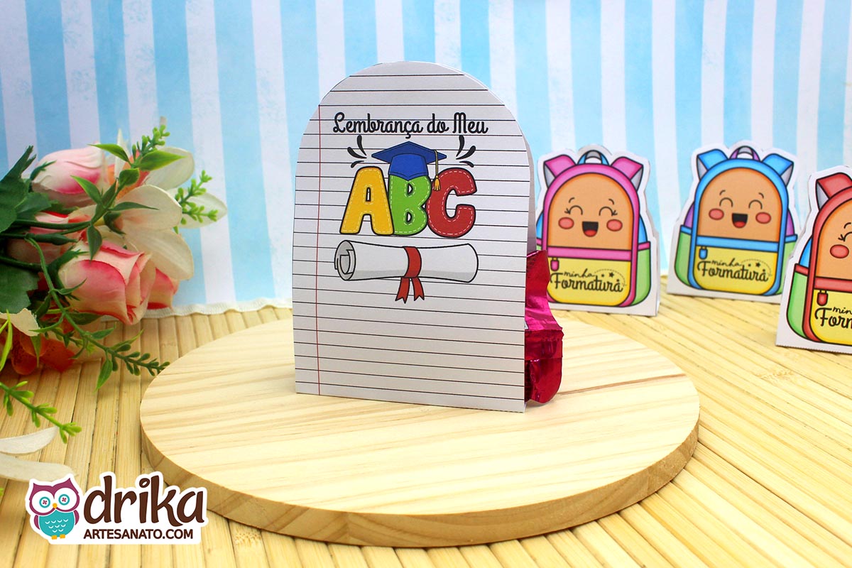 Porta-bombom formatura ABC com "Lembrança do Meu ABC" e desenho de letras, capelo e diploma sobre fundo de caderno.