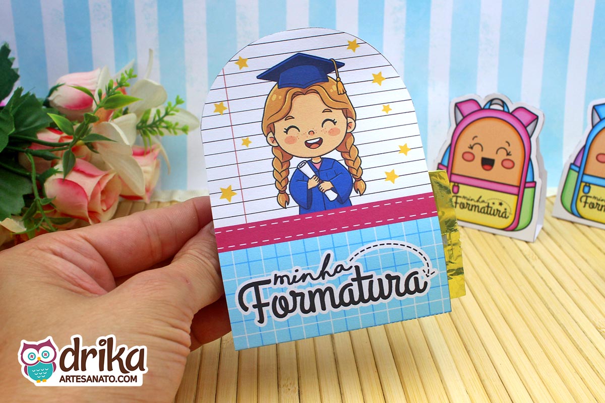 Porta-bombom Formatura ABC com menina de cabelo castanho, beca azul e fundo de caderno com estrelas amarelas.