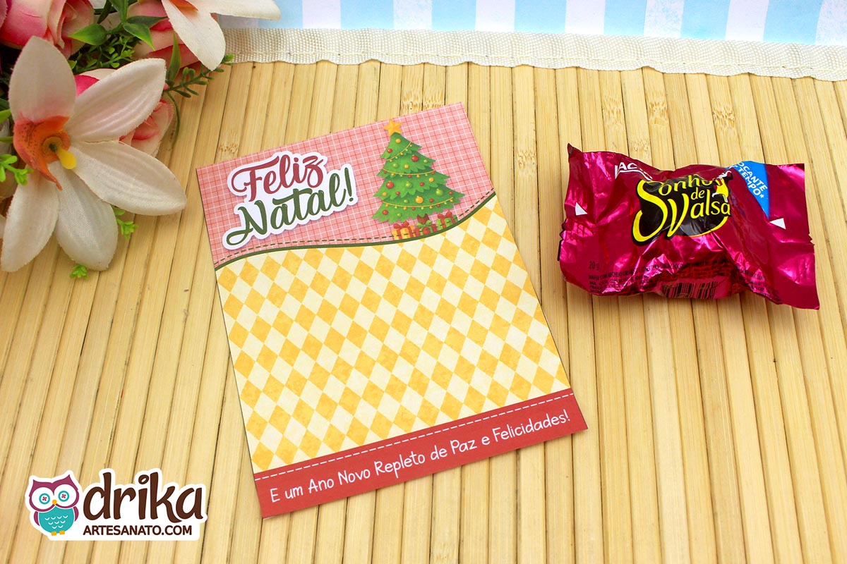 Cartão porta-bombom de Natal com fundo xadrez rosa, árvore verde decorada e bombom Sonho de Valsa ao lado.
