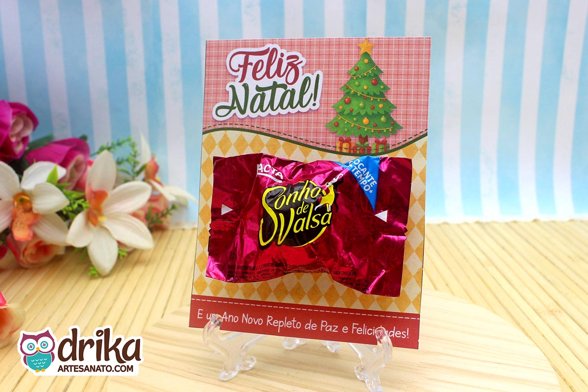 Cartão porta-bombom de Natal com bombom Sonho de Valsa encaixado, árvore verde e fundo xadrez rosa.