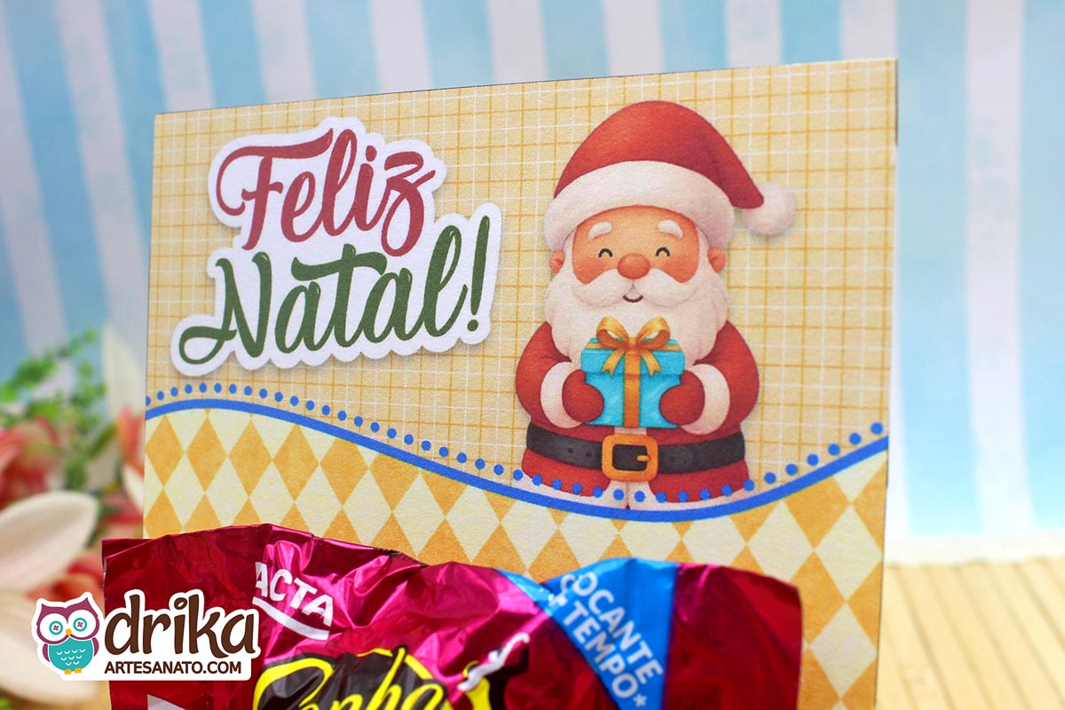 Close-up do cartão porta-bombom de Papai Noel com mensagem "Feliz Natal!" e bombom Sonho de Valsa.