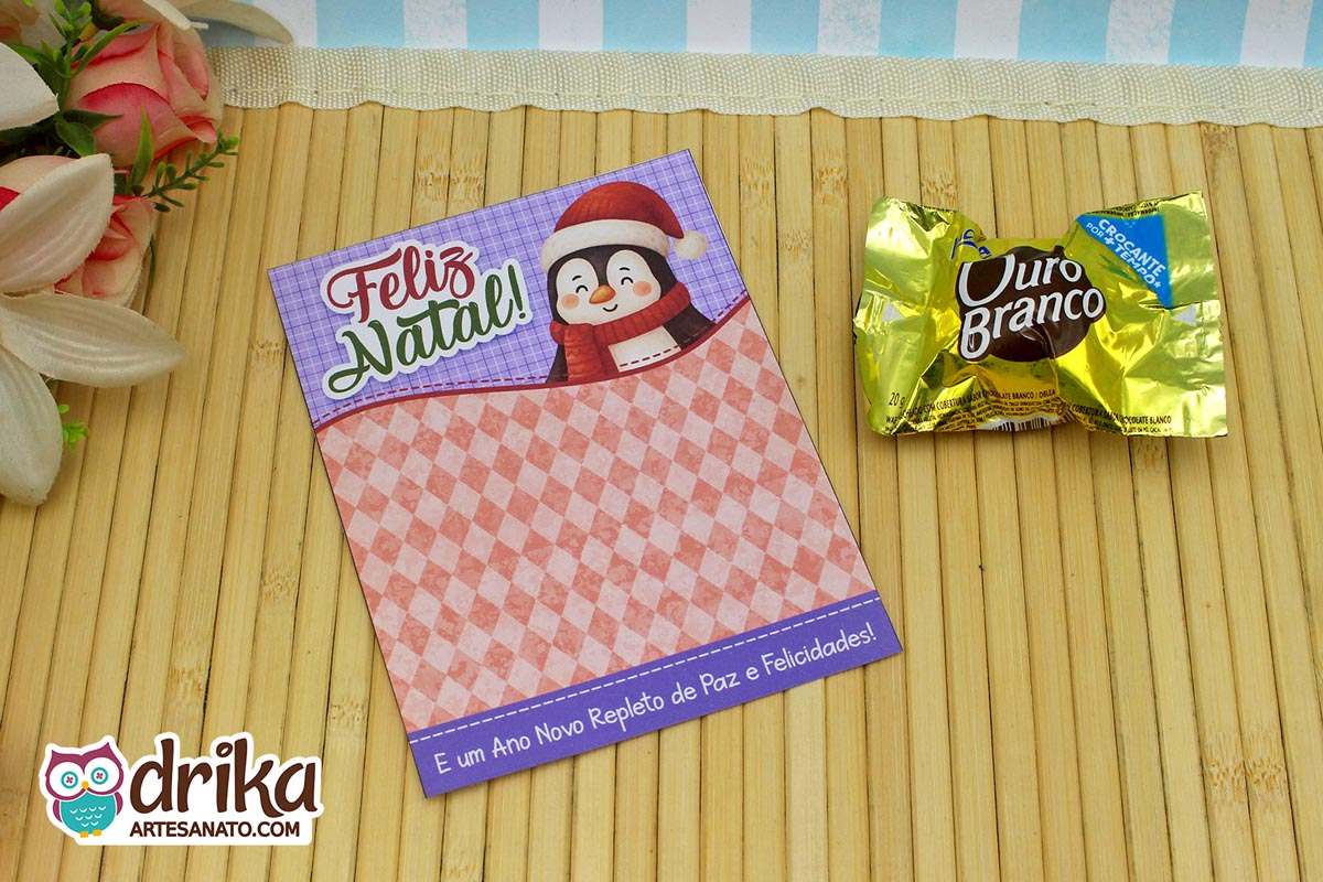 Cartão porta-bombom de Natal com pinguim fofo, mensagem "Feliz Natal!" e bombom Ouro Branco ao lado em fundo de madeira.