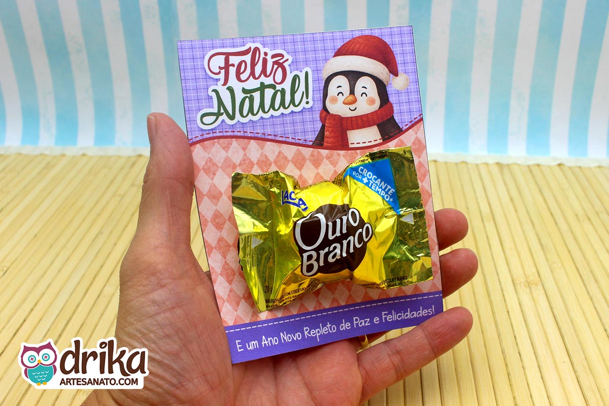 Mão segurando cartão porta-bombom de pinguim com bombom Ouro Branco, mostrando detalhes do design e mensagem.